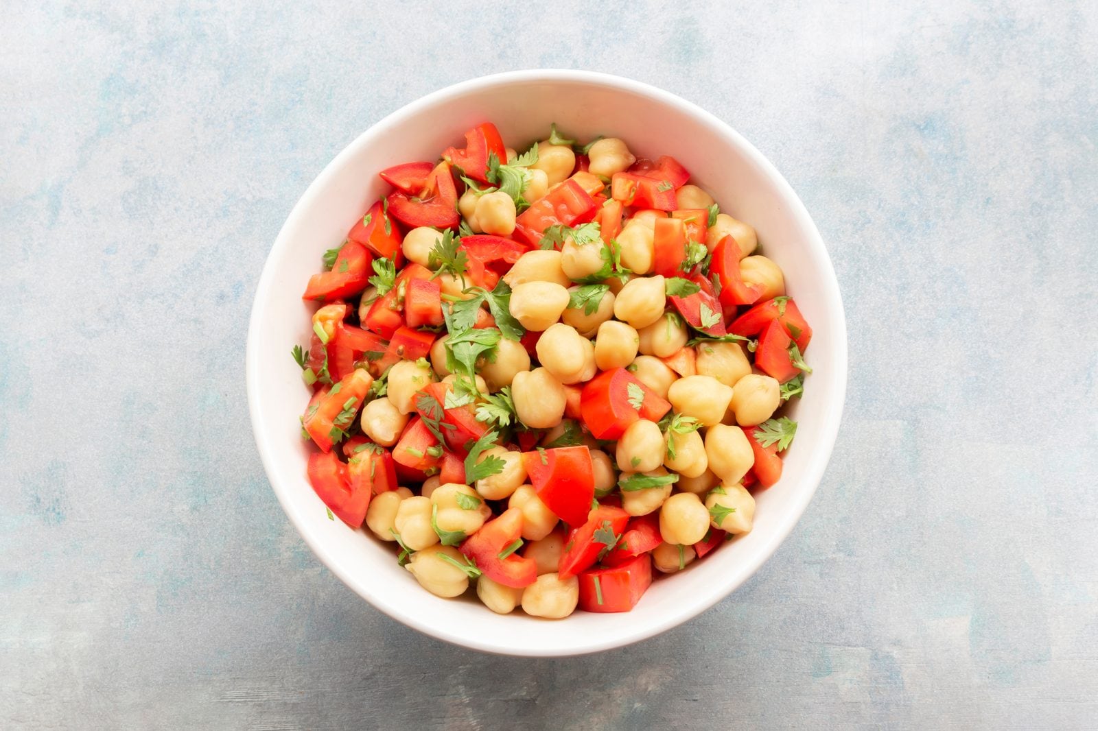 Kichererbsensalat mit Tomatenwürfeln und Koriander in einer weißen Schüssel auf blauem Holz
