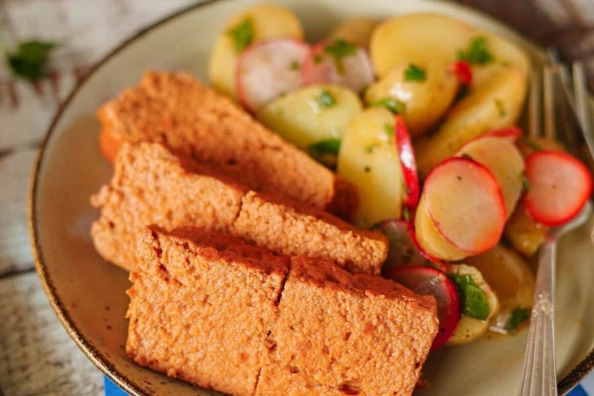 Selbstgemachter veganer Leberkäse in Scheiben mit Kartoffelsalat und Radieschen auf einem Teller