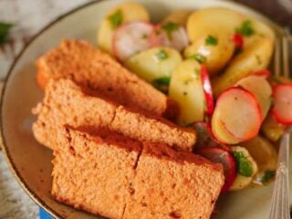 Selbstgemachter veganer Leberkäse in Scheiben mit Kartoffelsalat und Radieschen auf einem Teller