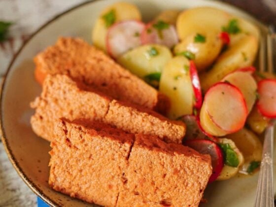 Selbstgemachter veganer Leberkäse in Scheiben mit Kartoffelsalat und Radieschen auf einem Teller