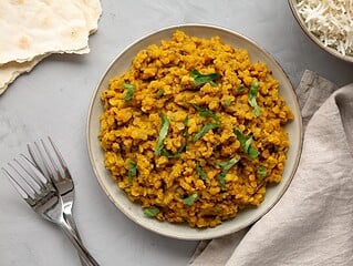 Rotes Linsen-Dal mit Basmatireis und frischem Koriander auf einem Teller, daneben Fladenbrot