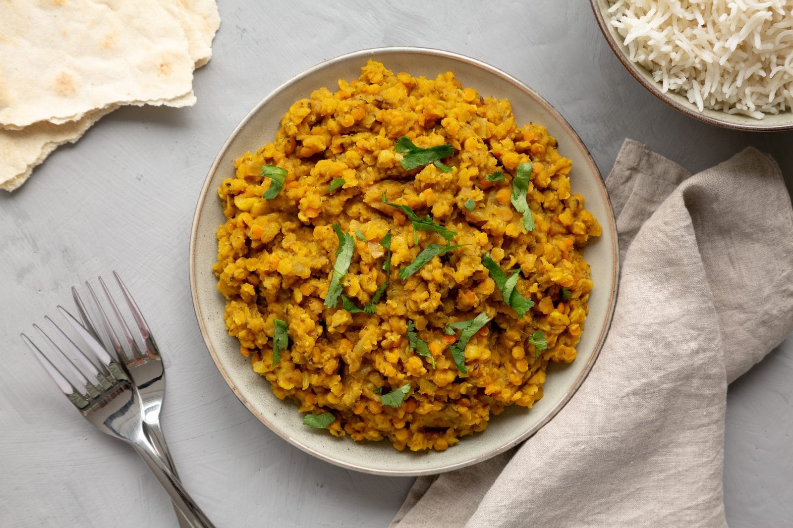 Rotes Linsen-Dal mit Basmatireis und frischem Koriander auf einem Teller, daneben Fladenbrot