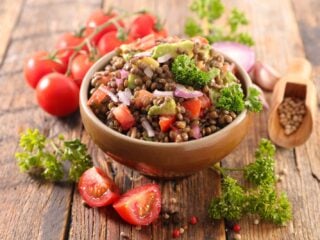 Veganer Linsensalat mit Kirschtomaten, roter Zwiebel und Petersilie in einer Holzschale auf rustikalem Tisch