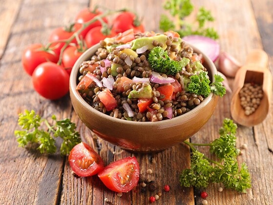 Veganer Linsensalat mit Kirschtomaten, roter Zwiebel und Petersilie in einer Holzschale auf rustikalem Tisch