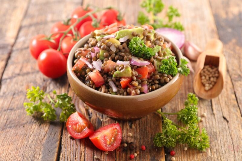 Veganer Linsensalat mit Kirschtomaten, roter Zwiebel und Petersilie in einer Holzschale auf rustikalem Tisch