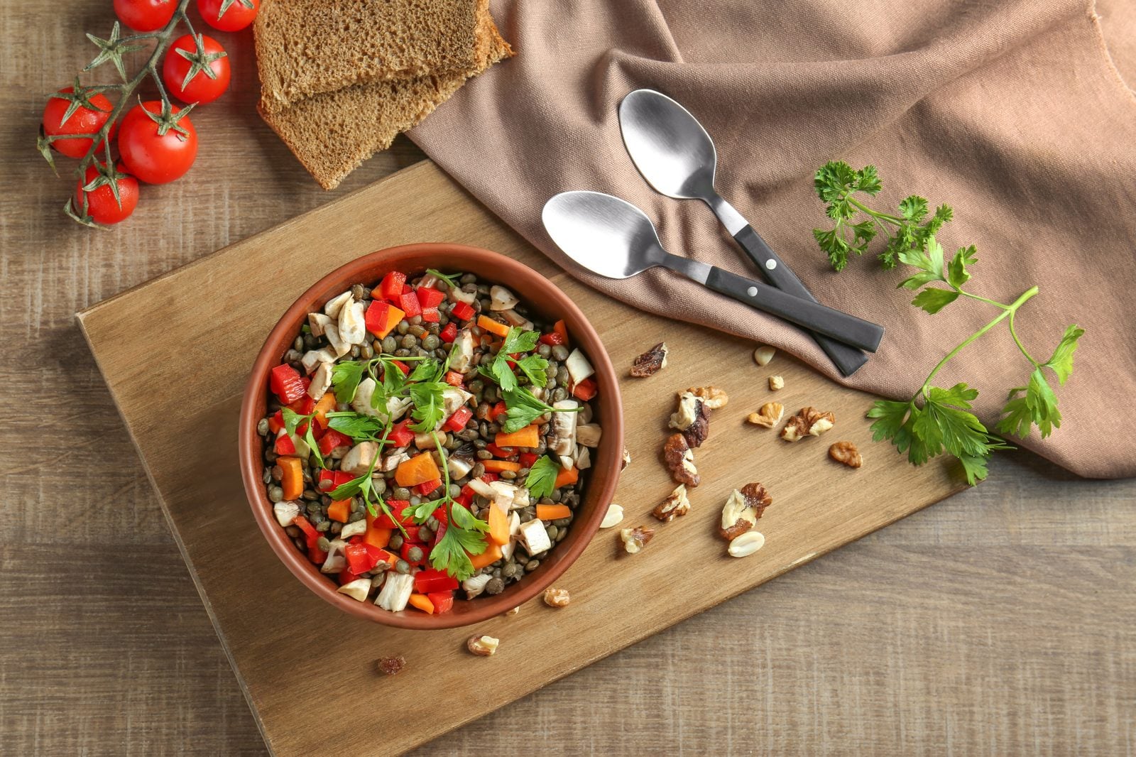 Linsensalat mit Tomaten, Petersilie und Walnüssen in einer Holzschale auf einem Holzbrett, daneben Löffel und Brot