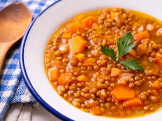 Vegane Linsensuppe mit Tellerlinsen, Karottenwürfeln und Petersilie in einer weißen Emailleschüssel