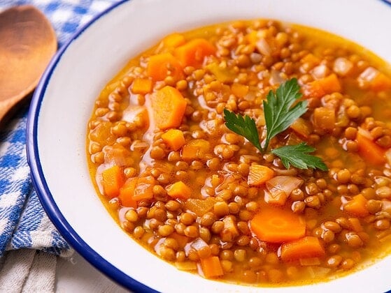 Vegane Linsensuppe mit Tellerlinsen, Karottenwürfeln und Petersilie in einer weißen Emailleschüssel