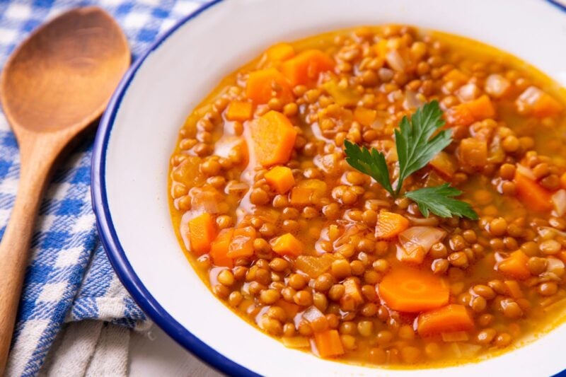 Vegane Linsensuppe mit Tellerlinsen, Karottenwürfeln und Petersilie in einer weißen Emailleschüssel