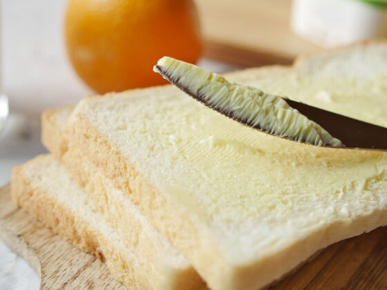Ein Messer streicht helles Streichfett auf eine Scheibe Toastbrot