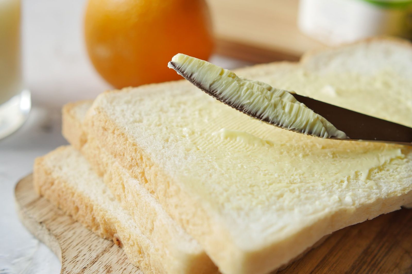 A knife spreading pale margarine on a slice of white toast