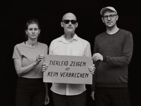 Moby hält zwischen Anna Schubert und Hendrik Haßel ein Pappschild mit der Aufschrift Tierleid zeigen ist kein Verbrechen