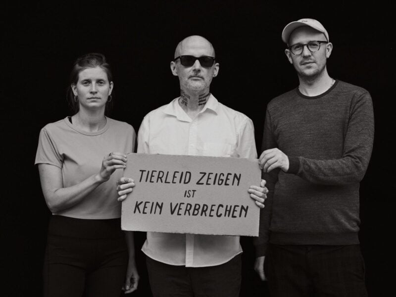 Moby hält zwischen Anna Schubert und Hendrik Haßel ein Pappschild mit der Aufschrift Tierleid zeigen ist kein Verbrechen