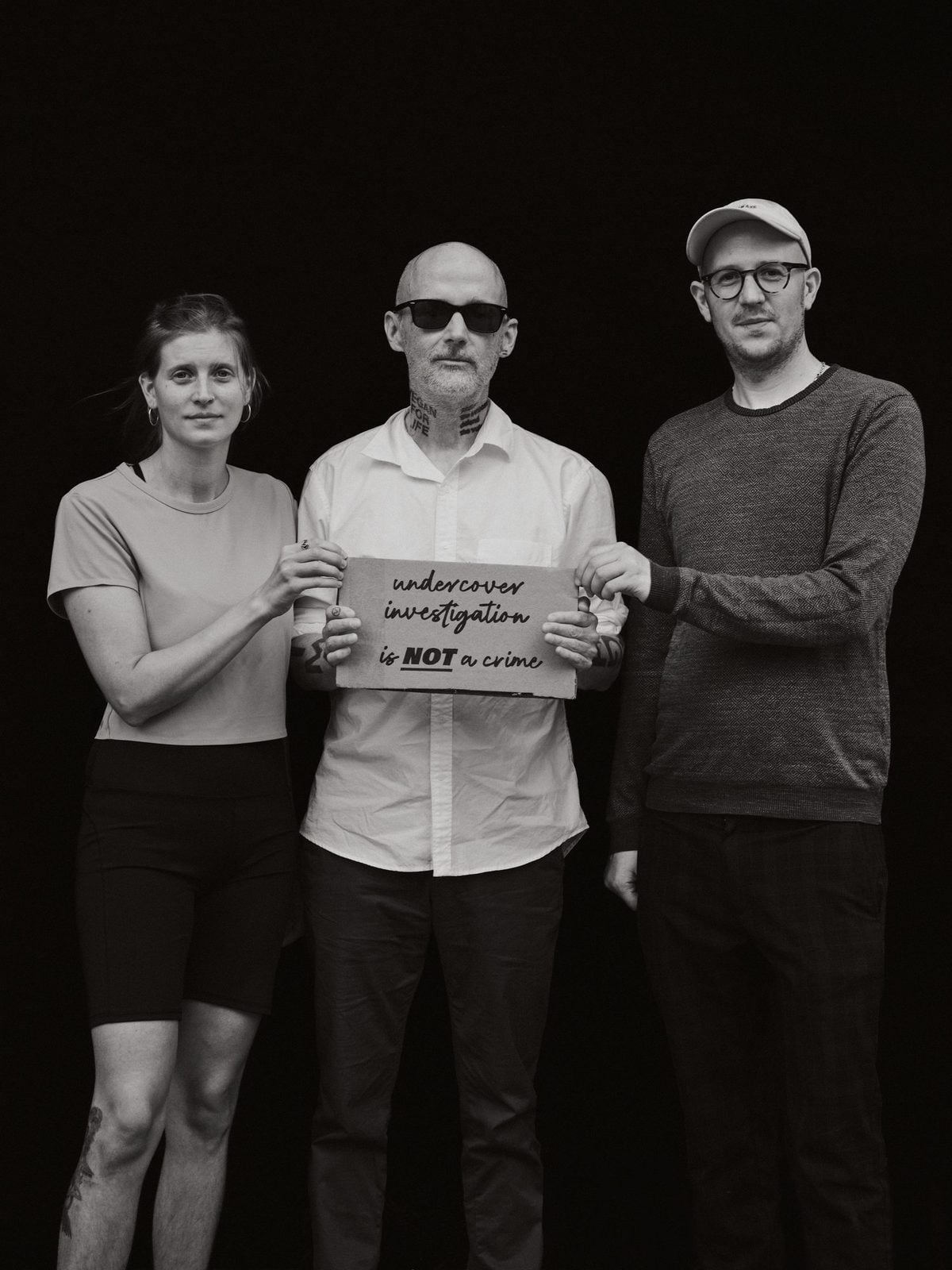 Anna Schubert, Moby und Hendrik Haßel stehen vor schwarzem Hintergrund, Moby hält ein Protestschild