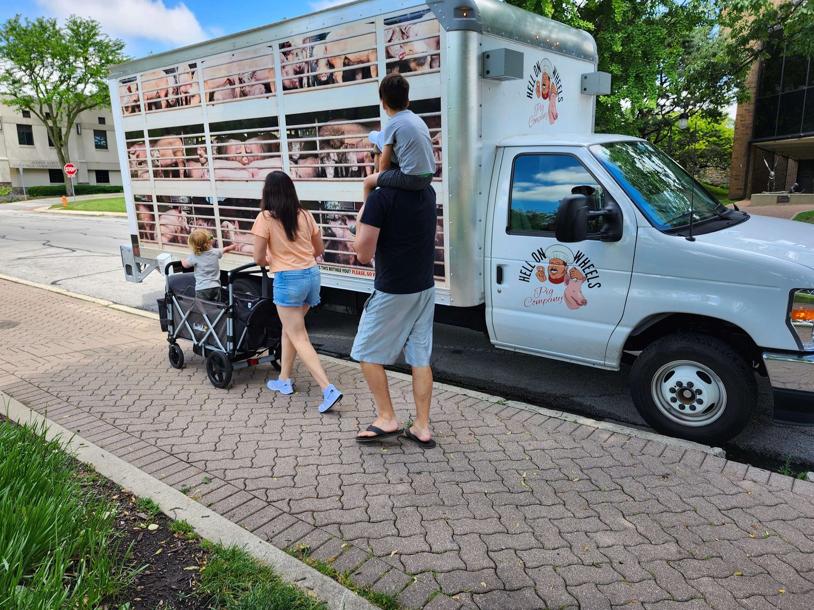 Familie mit Kindern vor einem Lkw, der einem Schweinetransporter nachempfunden ist