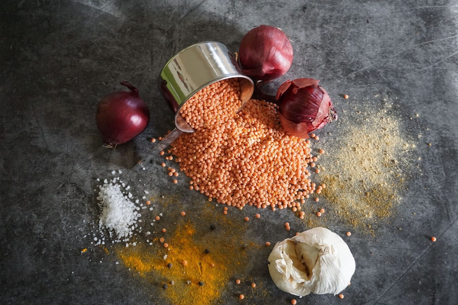 Rote Linsen, rote Zwiebeln, Knoblauch und Gewürze auf dunklem Untergrund von oben