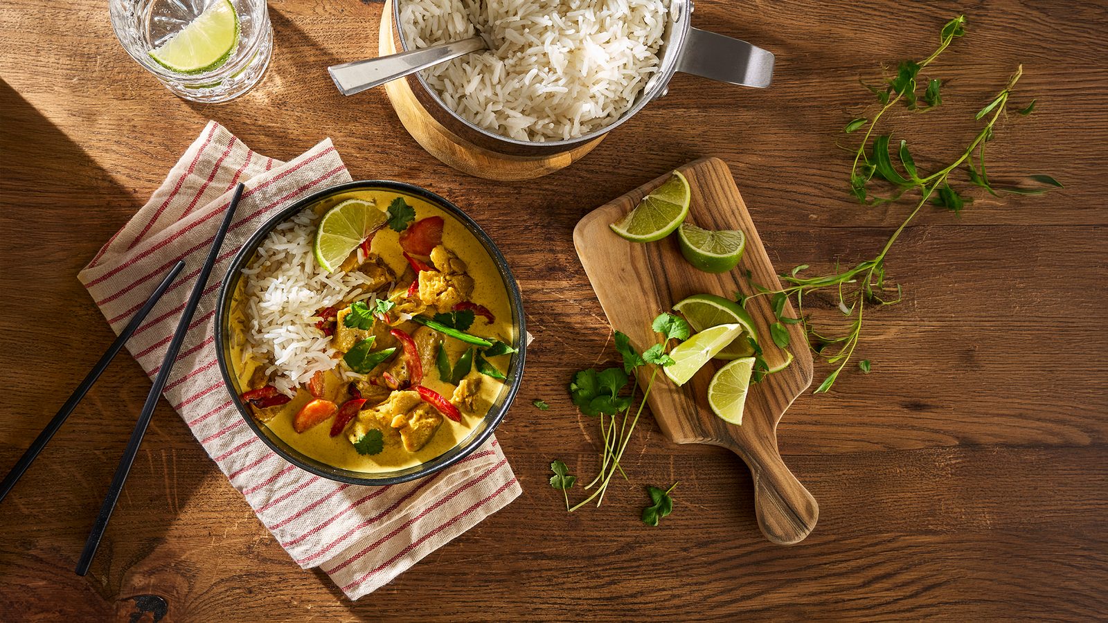 Schüssel mit veganem Curry aus Mühlen Chunks Indian Curry, Reis, Paprika und Limette auf einem Holztisch
