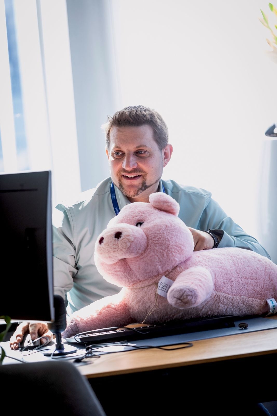 Sebastian Everding an seinem Schreibtisch mit einem großen rosa Plüschschwein auf dem Schoß