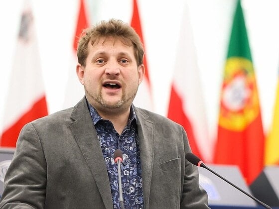 Sebastian Everding speaking at the rostrum in the plenary chamber of the European Parliament, flags of the member states in the background
