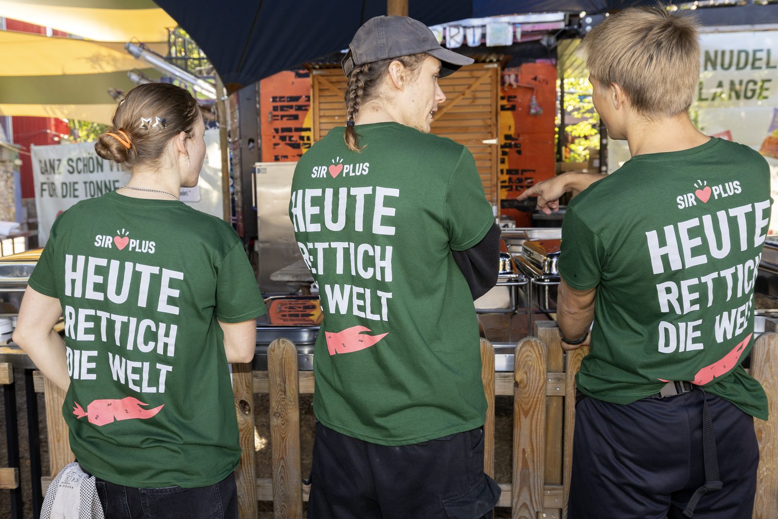 Drei Helfer:innen in grünen Shirts mit der Aufschrift Heute Rettich die Welt