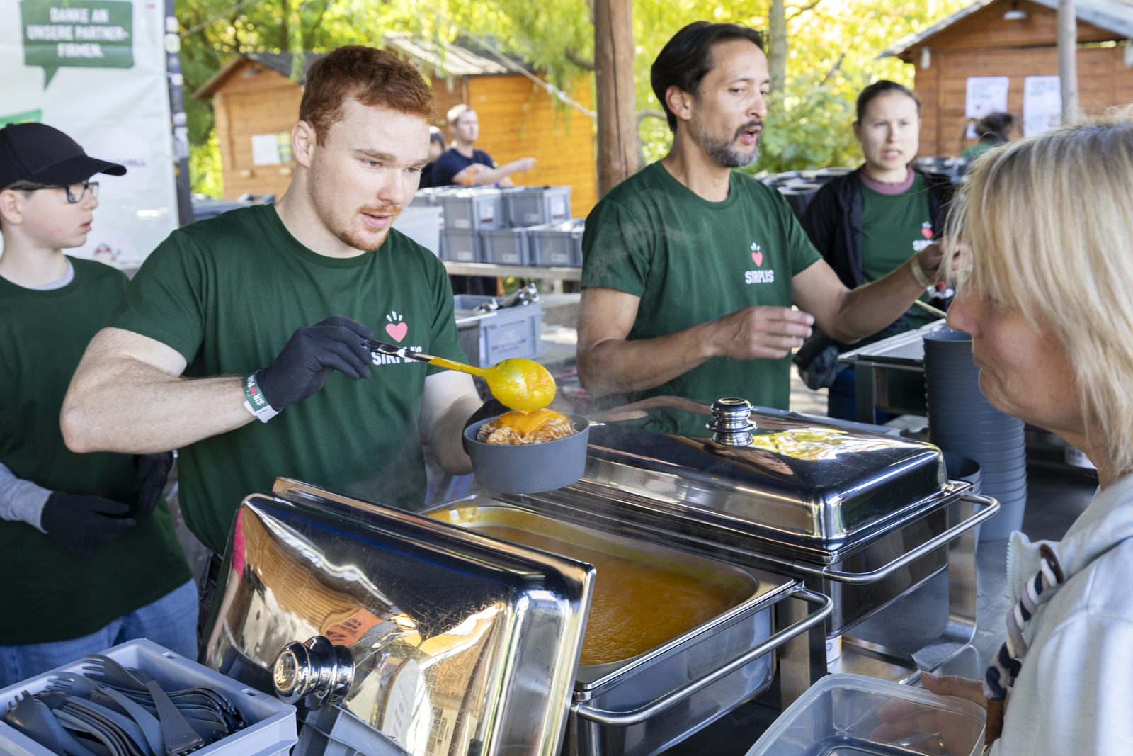 Freiwillige in grünen Shirts kochen an großen Töpfen