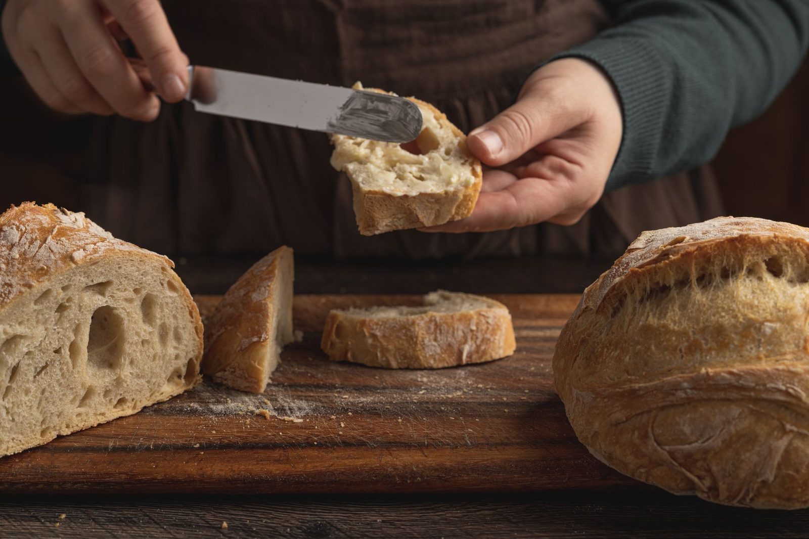 Two hands spreading a pale spread on a slice of rustic sourdough bread
