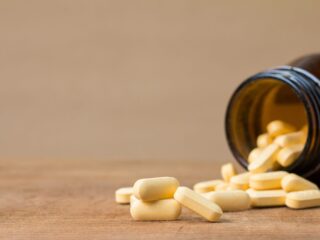 Gelbe Tabletten fallen aus einer umgekippten braunen Glasflasche auf einen Holztisch