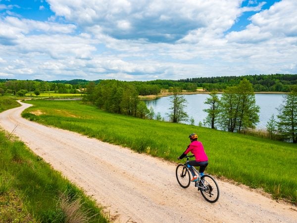 Radfahrerin auf einem Schotterweg durch grüne Wiesen an einem See