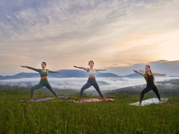 Drei Frauen üben Yoga auf einer Bergwiese bei Sonnenaufgang