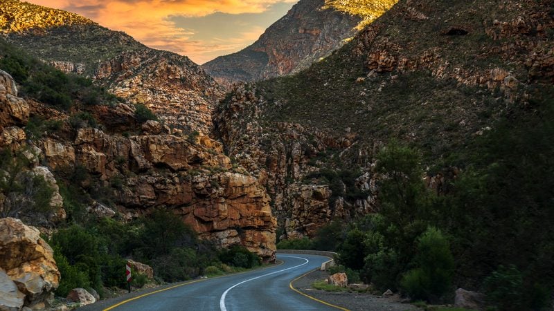 Landschaft in Kleine Karoo: Die Route 62 windet sich durch felsige Berge im Abendlicht