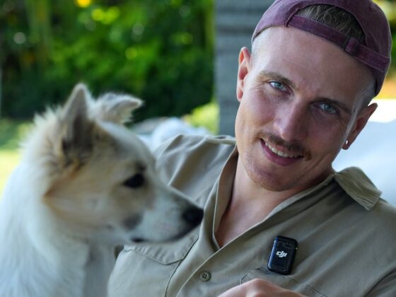 Yannick Haldenwanger lächelt neben einem weißen jungen Hund im Garten auf Bali