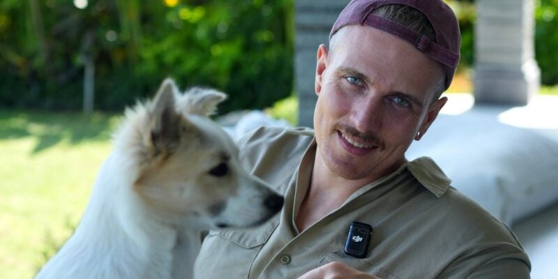 Yannick Haldenwanger lächelt neben einem weißen jungen Hund im Garten auf Bali