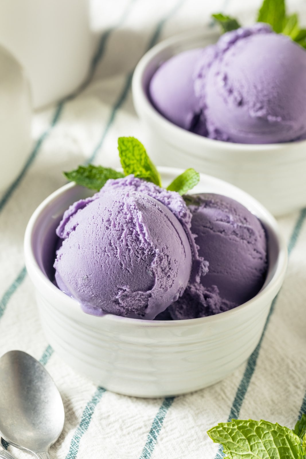 Zwei Kugeln violettes Ube-Eis in weißen Schälchen mit Minze