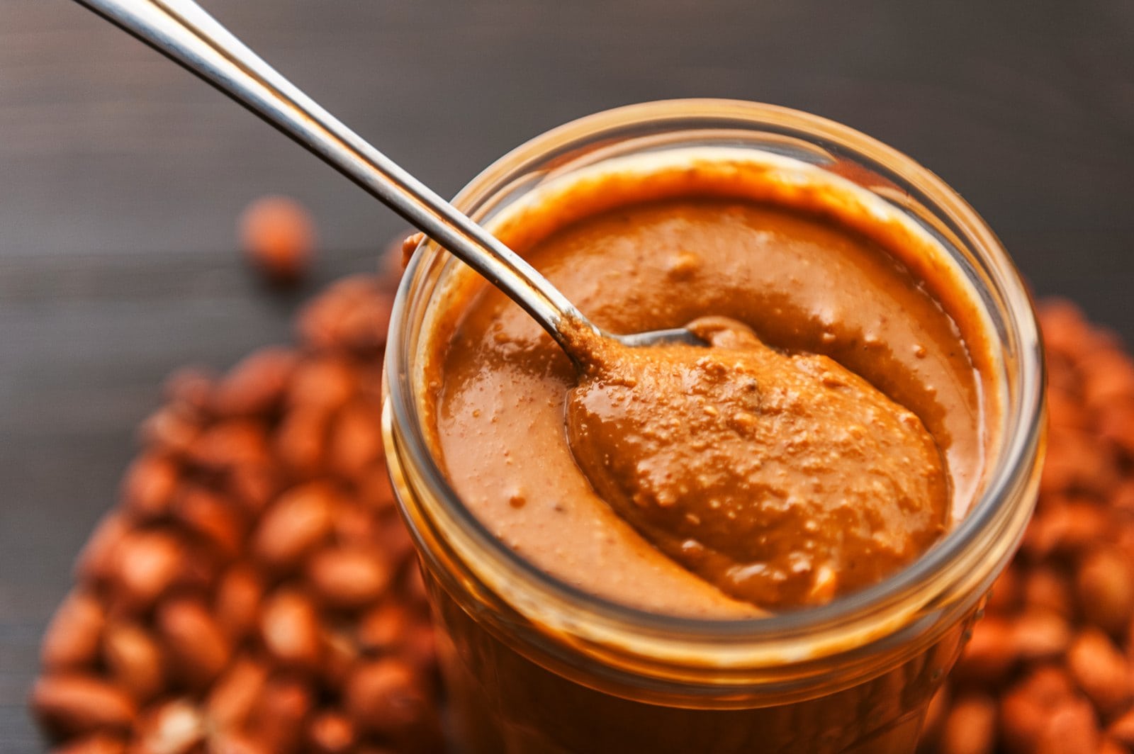 Glas Erdnussbutter mit Löffel: Nussmus ist eine der größten veganen Kalorienquellen