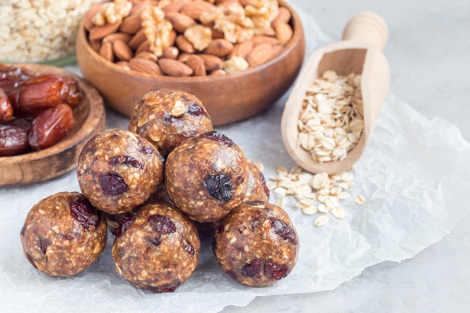 Energy Balls neben Schalen mit Mandeln, Datteln und Haferflocken auf Backpapier