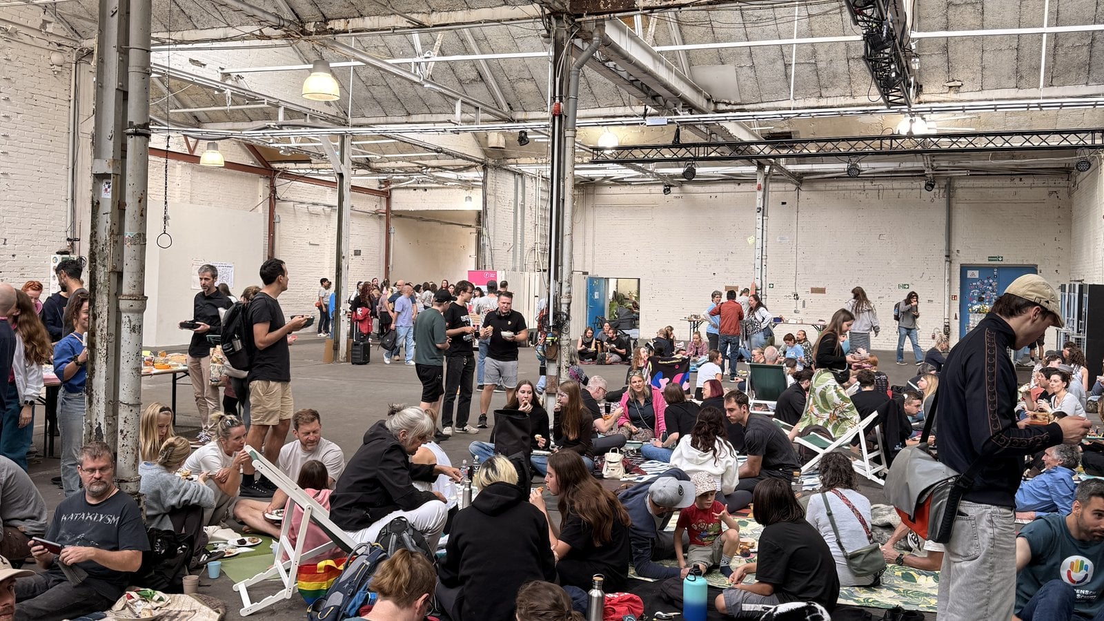 Menschen sitzen auf Picknickdecken in der Industriehalle beim veganen Mitbringbrunch in Berlin