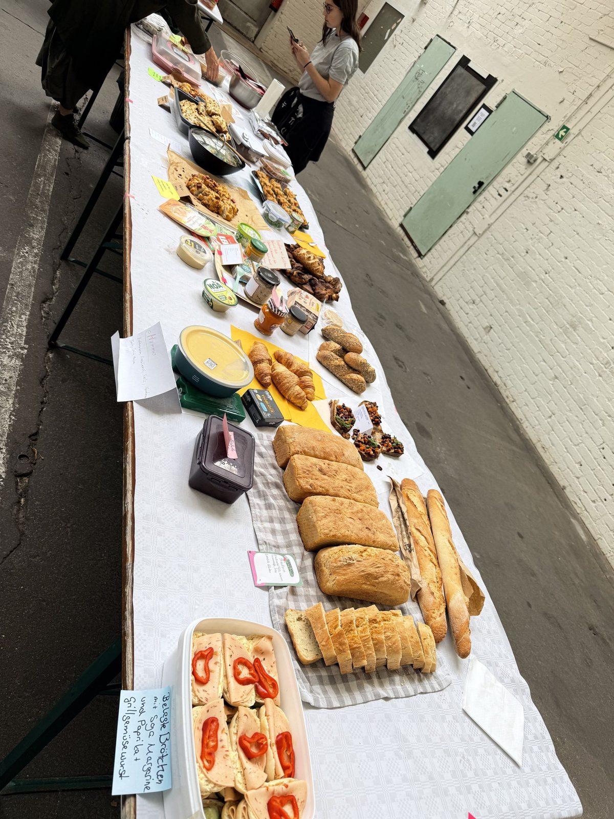 Lange Buffettafel mit selbst mitgebrachten veganen Gerichten und handgeschriebenen Zutatenschildern