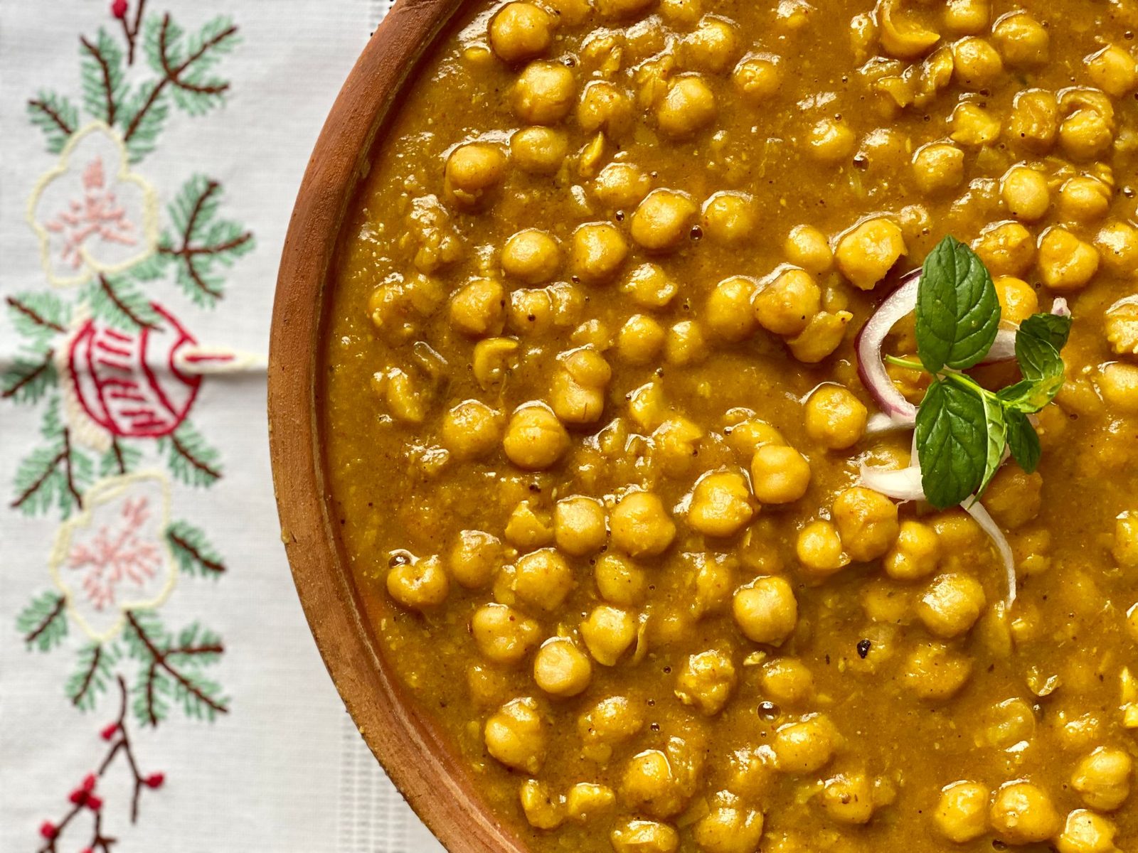 Close-up of chana masala, a chickpea curry, in a wooden bowl garnished with mint and onion