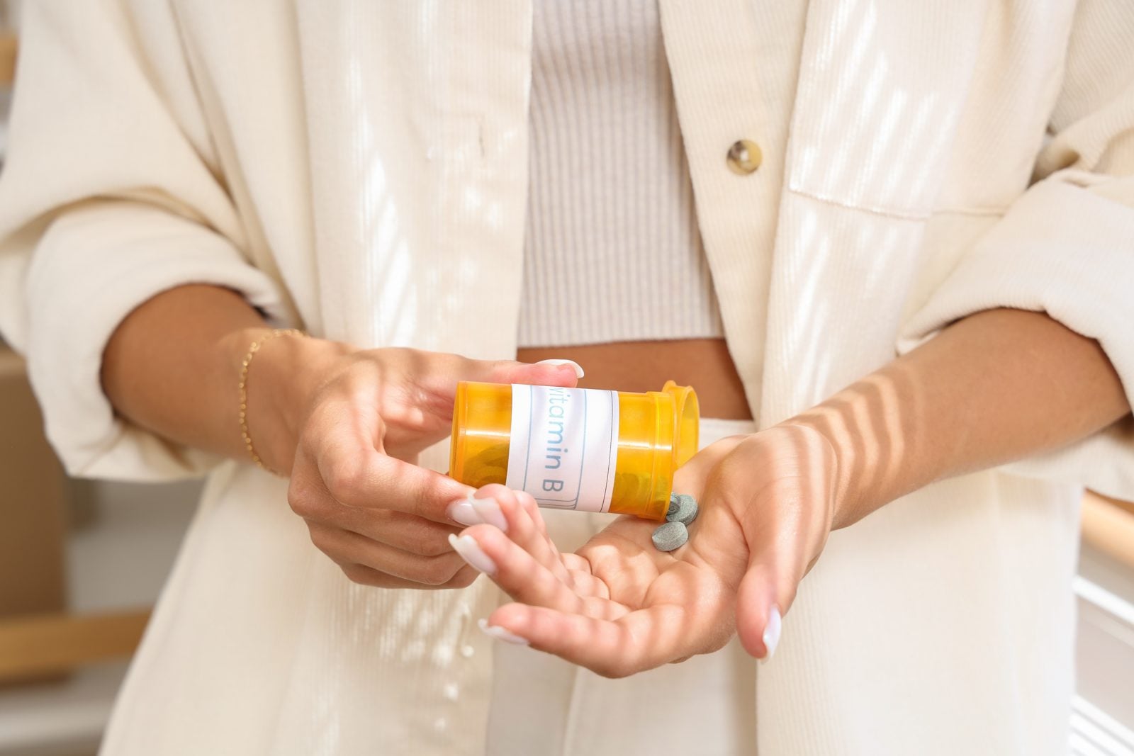 Frau schüttet Vitamin-B-Tabletten aus einer Dose in ihre Hand