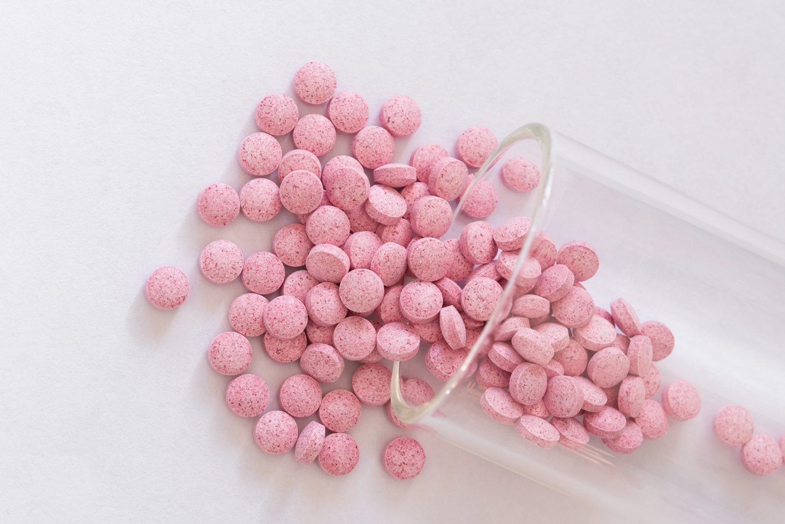 Rosa Vitamin-B12-Tabletten und ein Reagenzglas auf weißem Untergrund