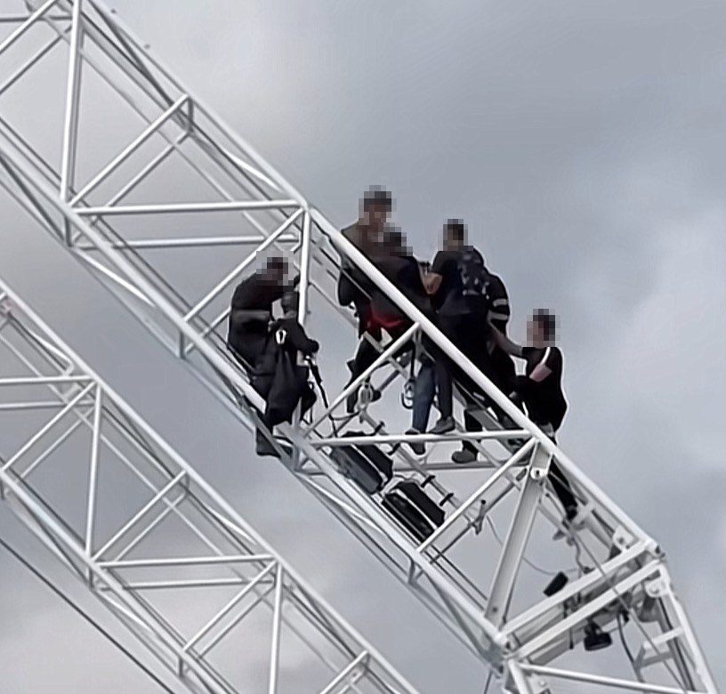 Several people standing close together on a white steel lattice structure against a cloudy sky