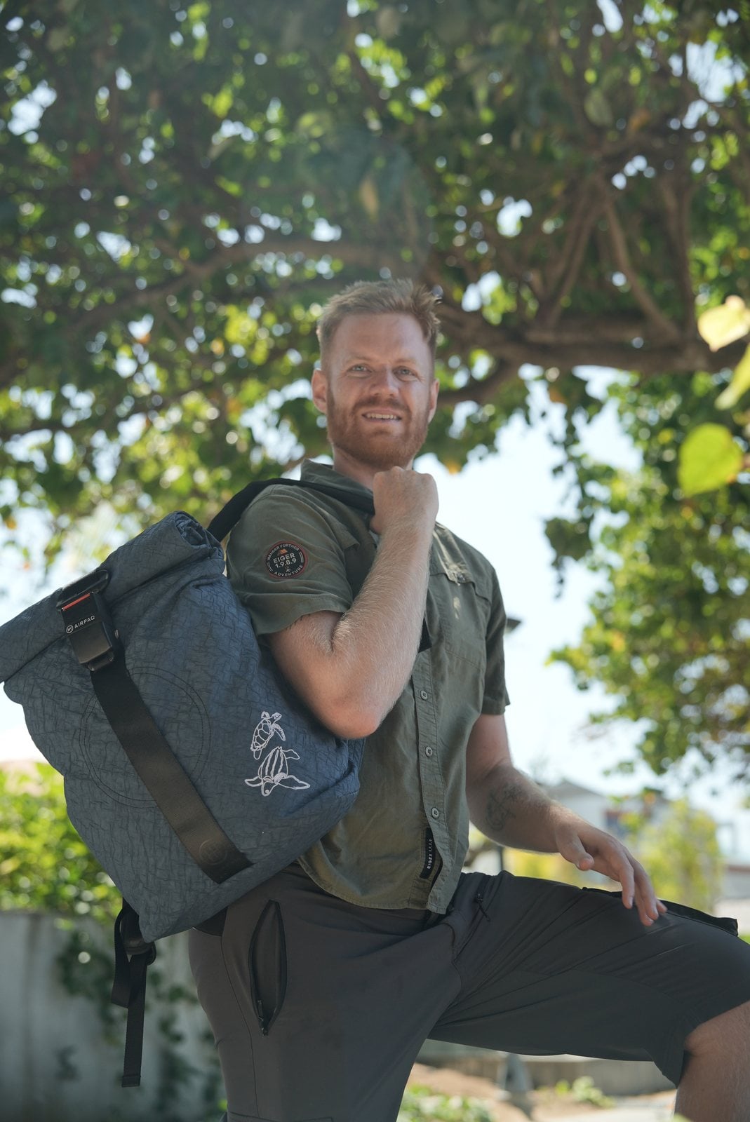 Manuel Bergmann mit dem Turtle Rolltop auf dem Rücken unter einem Baum