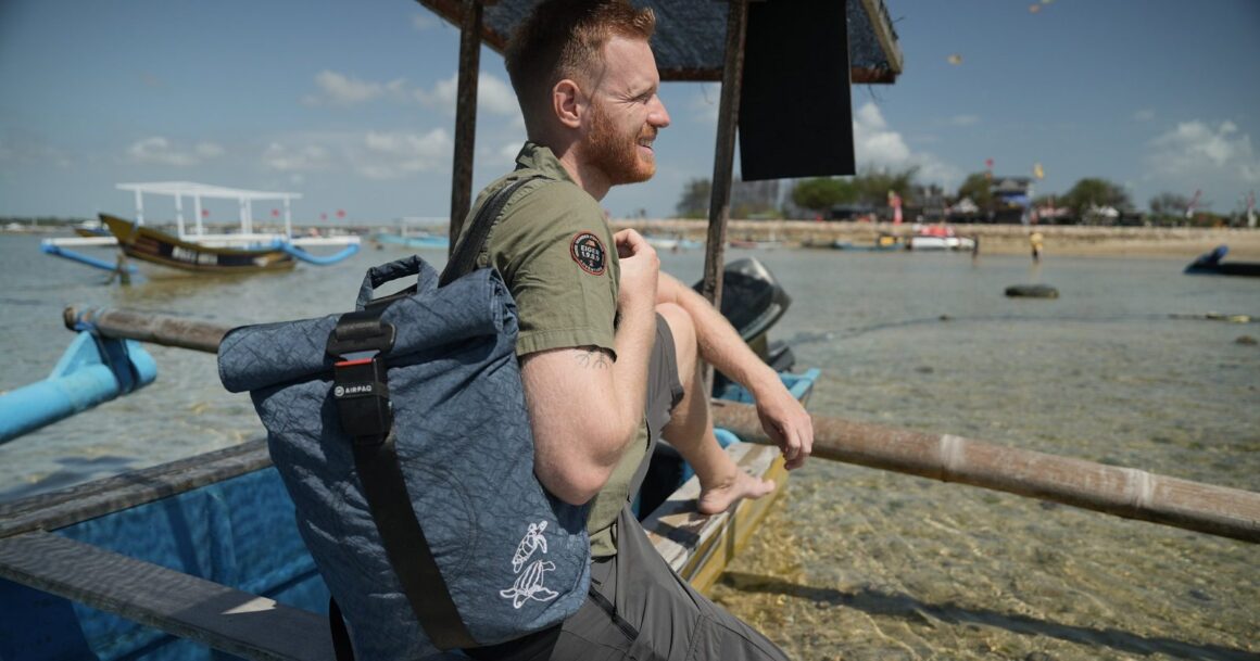 Manuel Bergmann sitzt mit dem Turtle Rolltop von Airpaq auf einem Boot und blickt aufs Meer