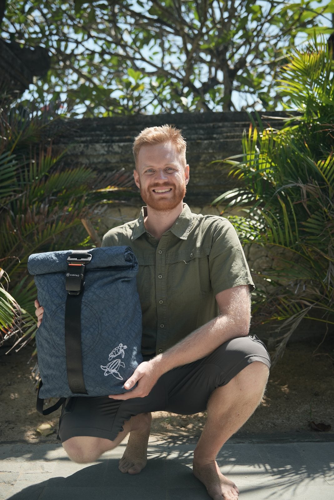 Manuel Bergmann kniet lächelnd neben dem blauen Turtle Rolltop von Airpaq