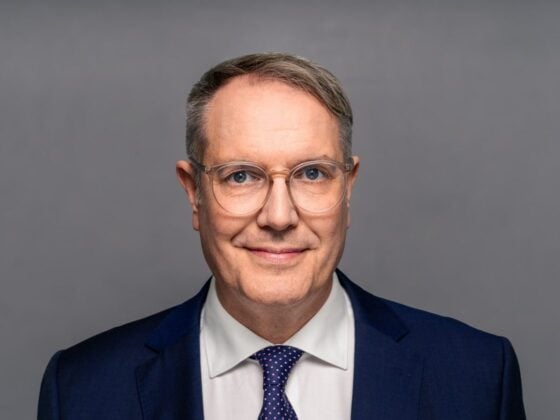 Porträt von Alexander Schweitzer (SPD) im dunkelblauen Anzug vor grauem Hintergrund