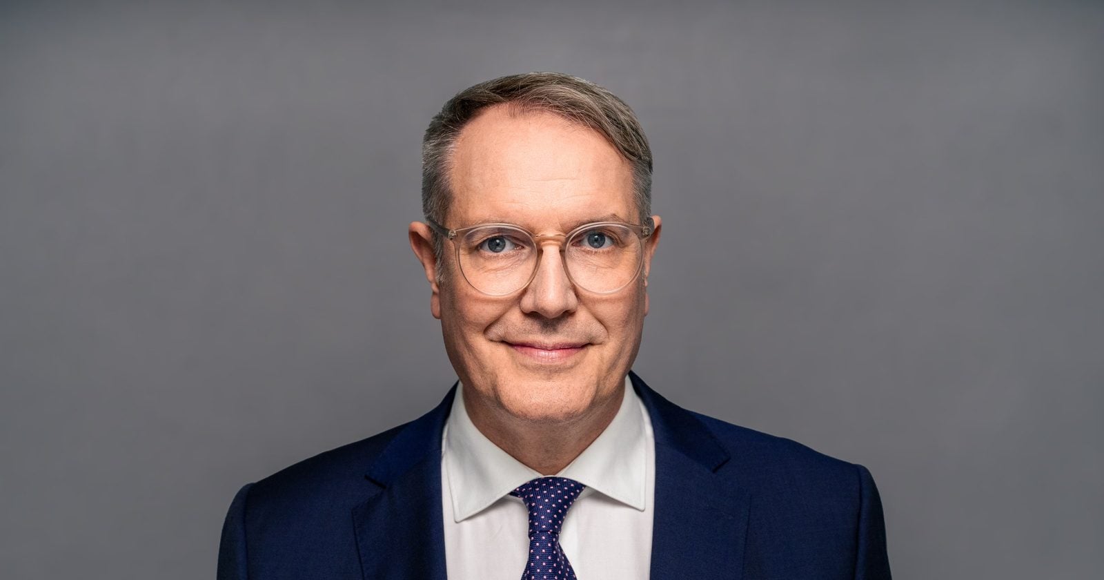 Porträt von Alexander Schweitzer (SPD) im dunkelblauen Anzug vor grauem Hintergrund