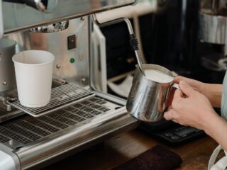Barista schäumt Haferdrink in einem Edelstahlkännchen an der Siebträgermaschine auf