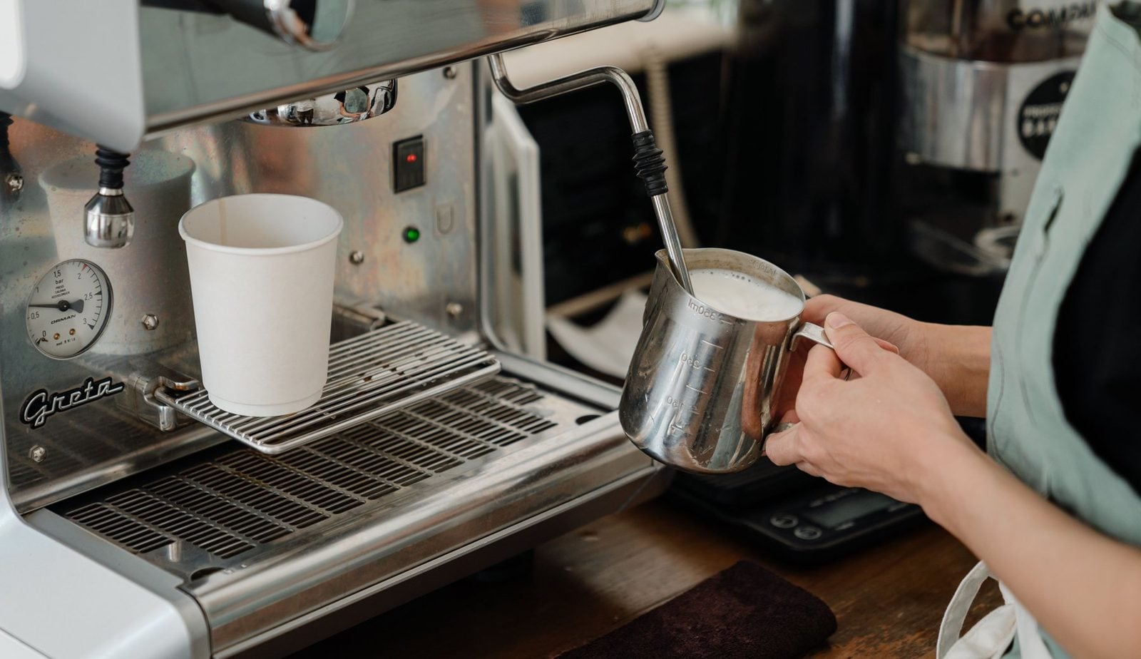 Barista schäumt Haferdrink in einem Edelstahlkännchen an der Siebträgermaschine auf