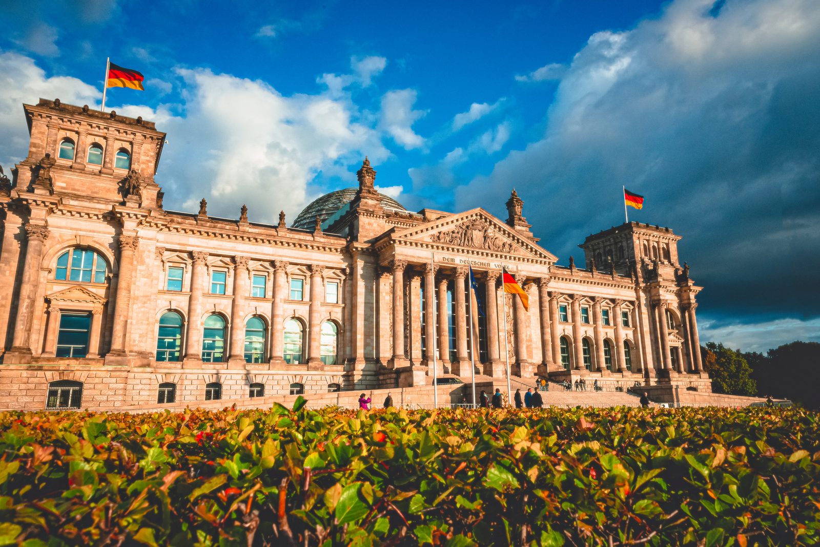 Das Reichstagsgebäude in Berlin mit Deutschlandfahnen vor blauem Himmel