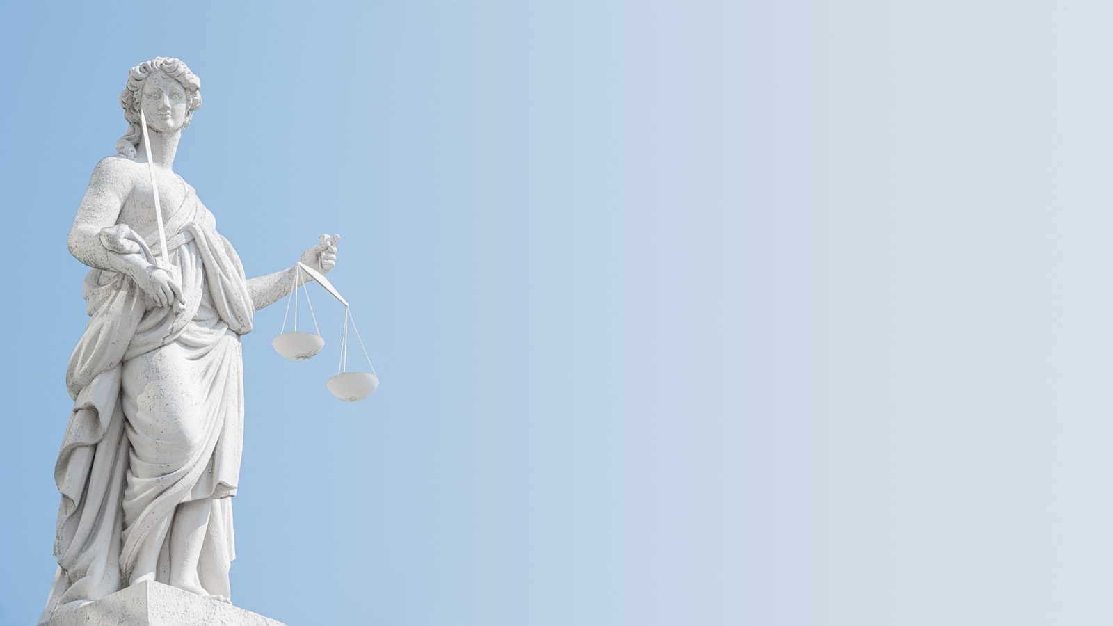 Justitia-Statue mit Waage und Schwert auf einem Dach in Potsdam vor blauem Himmel